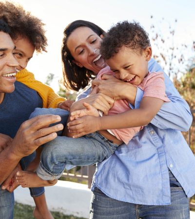 Young mixed race parents playing outdoors carrying their children in the garden